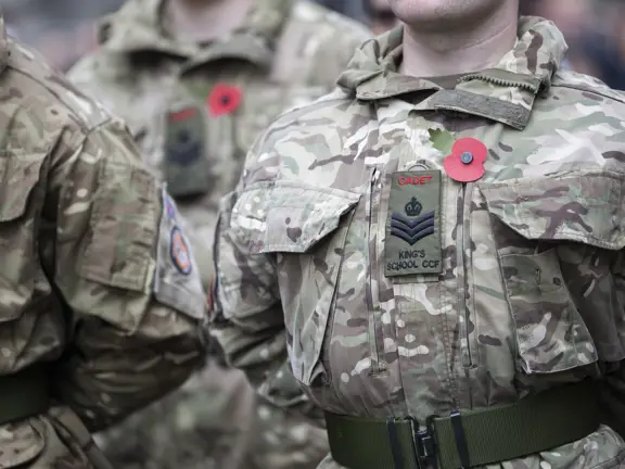 Close-up of Army Cadets in camouflage uniforms wearing red poppy pins for remembrance on their chests.